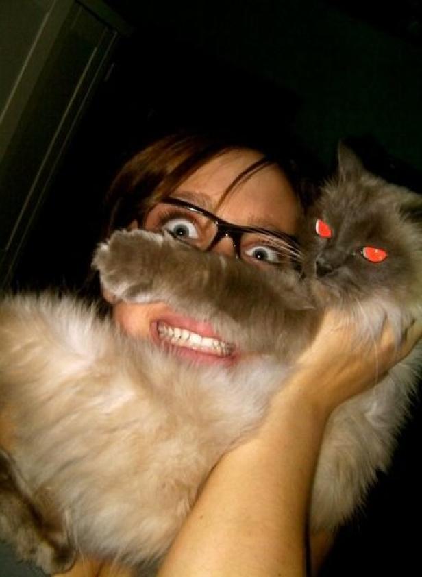 Eine Frau hält eine Katze vor ihr Gesicht und grinst in die Kamera.