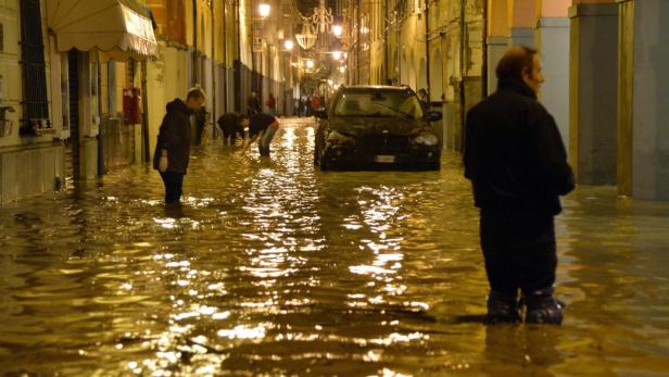 Eine überflutete Straße mit Menschen und einem Auto im Wasser.