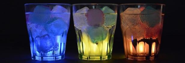 Drei Gläser mit Eiswürfeln, beleuchtet in den Farben Blau, Gelb und Orange.