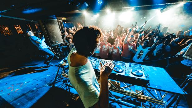 Ein DJ legt vor einer jubelnden Menge in einem Nachtclub auf.