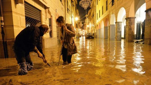 Zwei Personen waten durch eine überflutete Straße in einer Stadt.