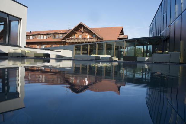 Ein Pool spiegelt ein Holzgebäude und moderne Architektur wider.