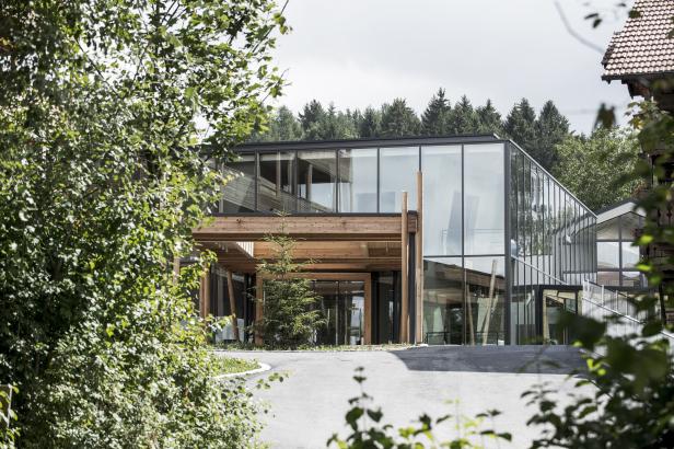 Ein modernes Gebäude mit viel Glas und Holzelementen, umgeben von Bäumen.