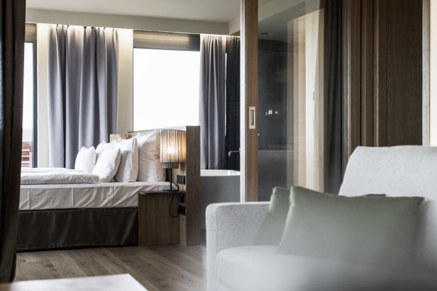 Ein modernes Hotelzimmer mit Bett, Sessel und Blick ins Badezimmer.