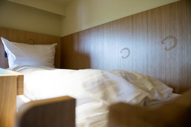 Ein Bett mit weißer Bettwäsche und einem hölzernen Kopfteil mit Hufeisenverzierungen.