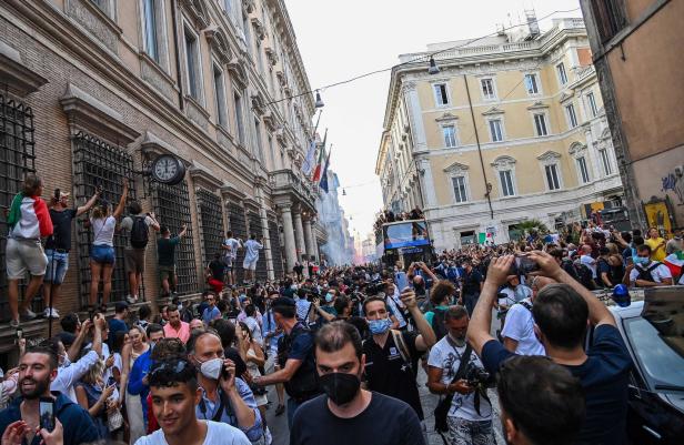 Eine Menschenmenge feiert auf einer Straße in Rom, einige klettern auf Gebäude.