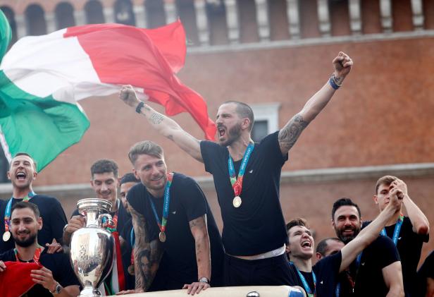 Italienische Fußballspieler feiern mit der Trophäe und der italienischen Flagge.