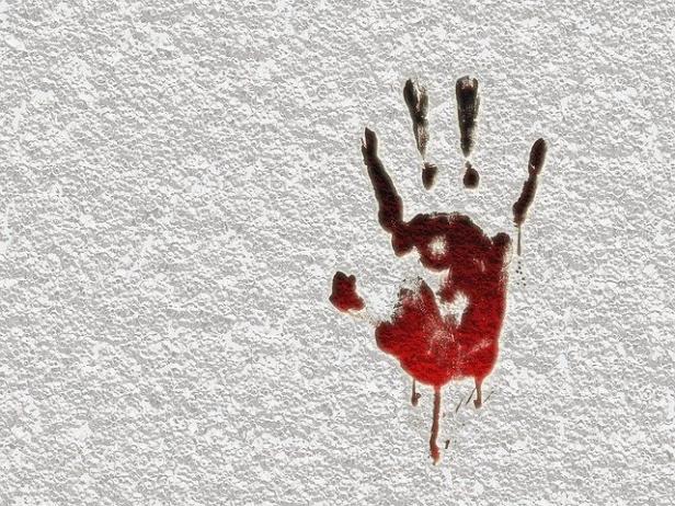 Ein blutiger Handabdruck mit Ausrufezeichen an einer weißen Wand.