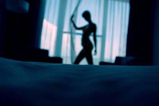 Der Schatten einer Frau steht am Fenster in einem abgedunkelten Raum.