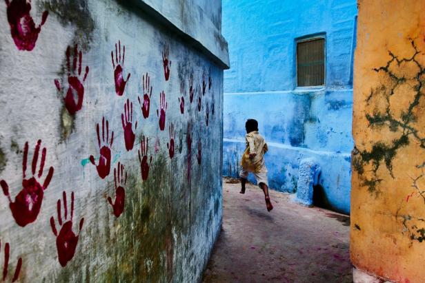 Ein Junge rennt barfuß durch eine Gasse mit blau gestrichenen Häusern in Indien.