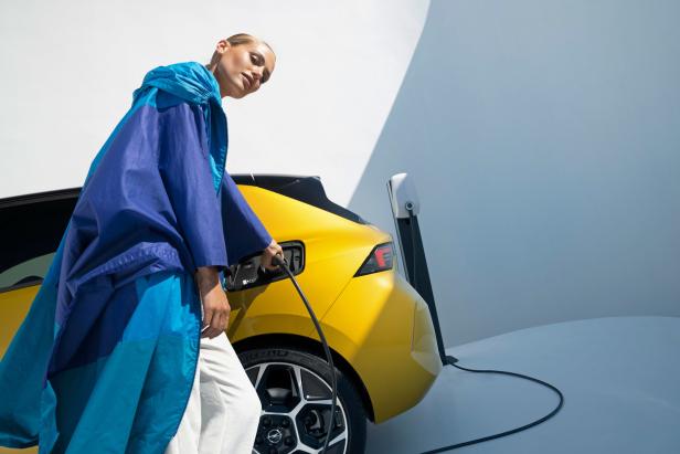 Eine Frau schließt ein gelbes Elektroauto an eine Ladestation an.
