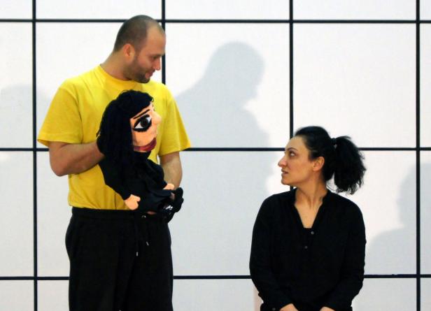 Ein Mann mit einer Handpuppe interagiert mit einer Frau vor einem weißen Hintergrund.