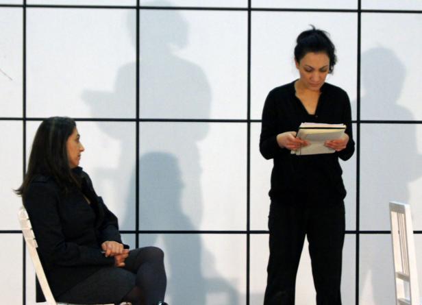 Eine Frau liest ein Skript, während eine andere Frau auf einem Stuhl sitzt.