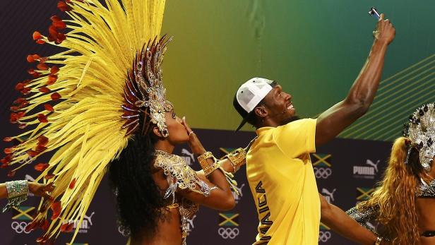 Usain Bolt macht ein Selfie mit einer Tänzerin in einem farbenprächtigen Kostüm.