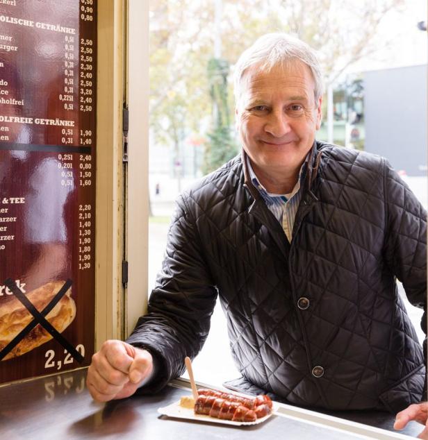 Ein Mann mittleren Alters steht an einem Imbissstand mit einer Portion Bratwurst.