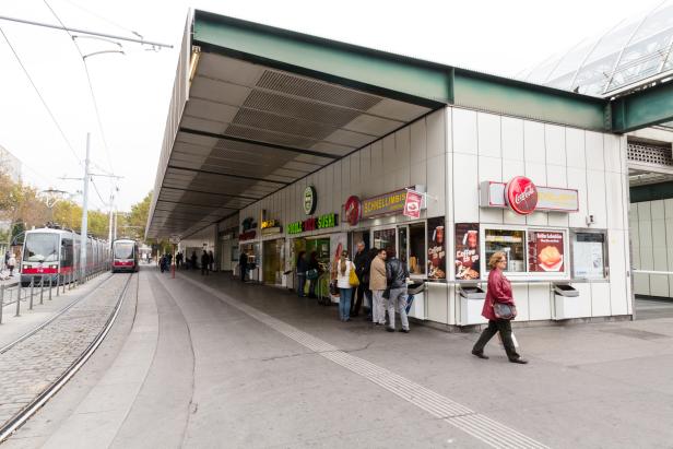 Eine Frau geht an einem Schnellimbiss am Europaplatz vorbei, während eine Straßenbahn einfährt.
