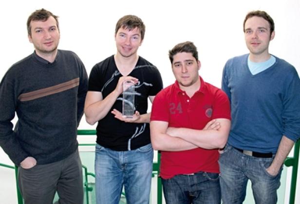 Vier Männer posieren für ein Foto, einer hält eine Trophäe.