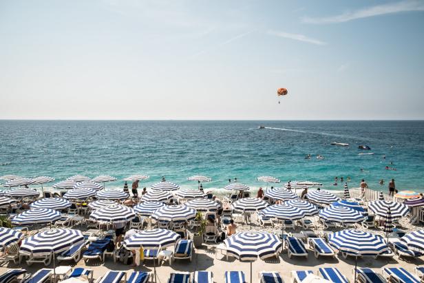 Ein Strand in Nizza mit blau-weiß gestreiften Sonnenschirmen und Badegästen.