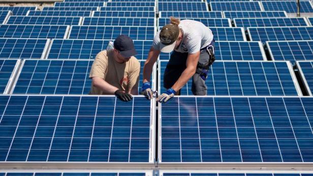Zwei Arbeiter installieren blaue Solarmodule auf einem Dach.