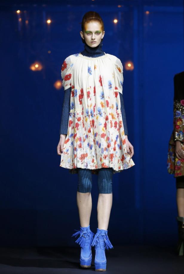 Ein Model präsentiert ein Kleid mit Blumenmuster, blaue Leggings und blaue Stiefel auf dem Laufsteg.