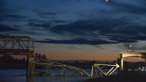 Eine teilweise eingestürzte Brücke über einem Fluss bei Dämmerung.