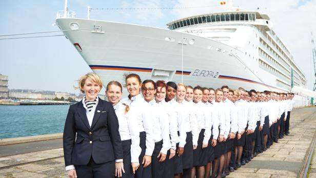 Eine Gruppe von Besatzungsmitgliedern steht vor dem Kreuzfahrtschiff „Europa 2“.