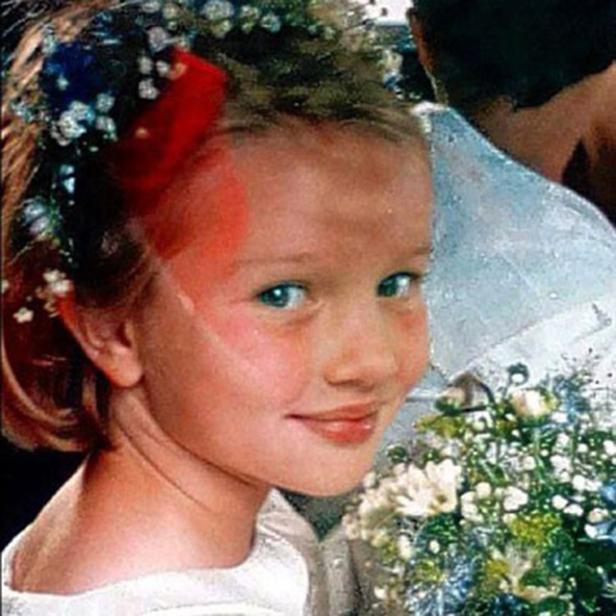 Ein junges Mädchen mit Blumenkranz und roter Schleife lächelt in die Kamera.