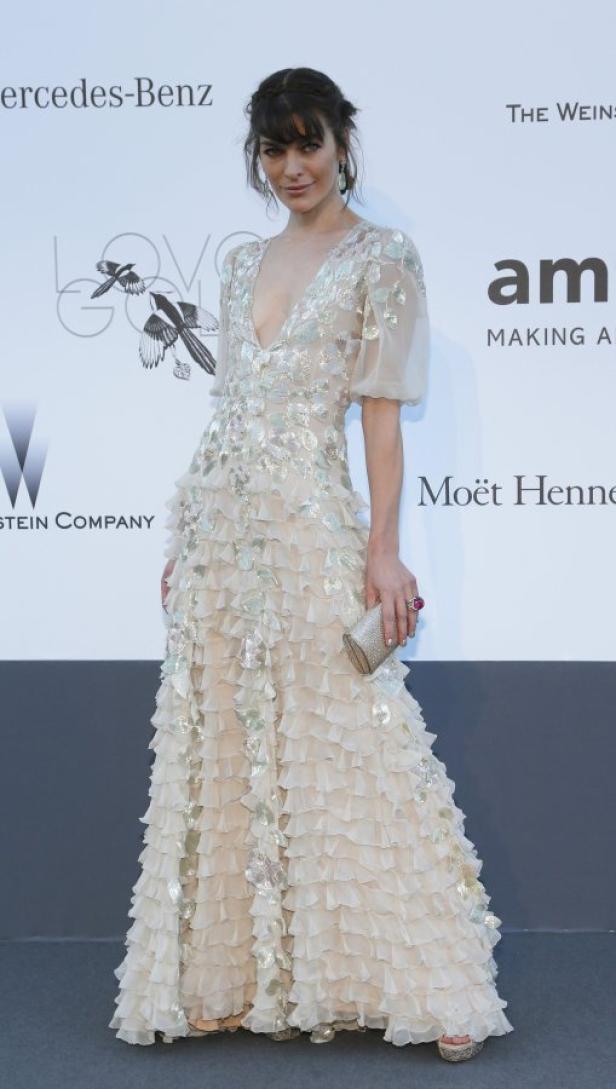 Milla Jovovich in einem langen, hellen Kleid mit Rüschen und silbernen Applikationen.