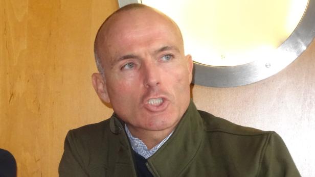 Ein Mann mit Glatze und grünem Jackett spricht.