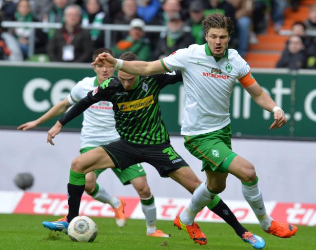 Ein Fußballspieler von Werder Bremen dribbelt den Ball, während er von einem Gegenspieler attackiert wird.