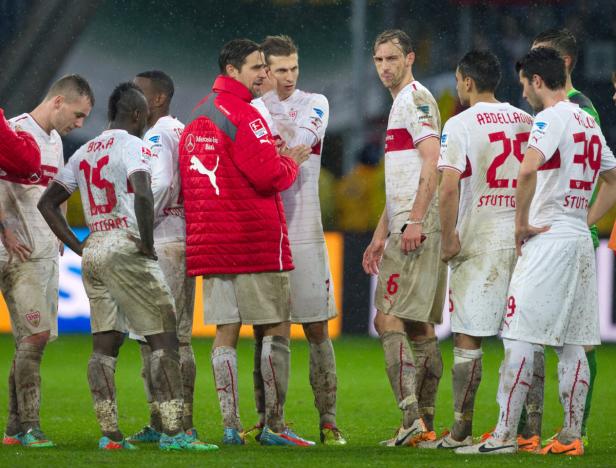 Eine Gruppe schlammverschmutzter Fußballspieler des VfB Stuttgart steht auf dem Rasen.