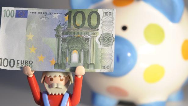 Eine Spielfigur hält einen 100-Euro-Schein vor einem Sparschwein.