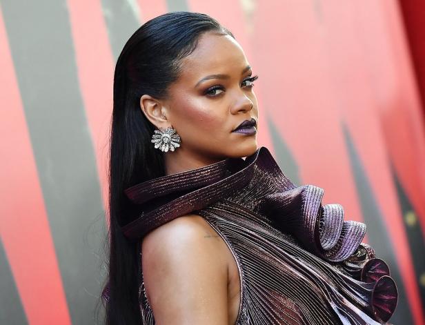 Rihanna steht mit einem Kleid im Metallic-Look vor einer schwarz-roten Wand.