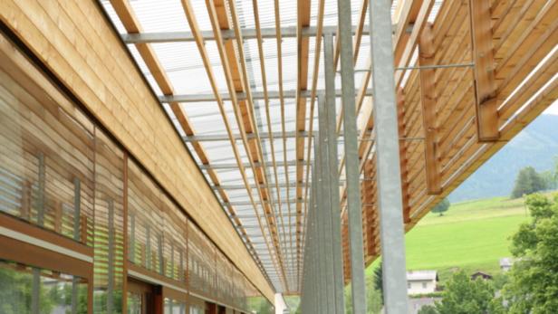 Die Holzfassade eines modernen Gebäudes mit einer transparenten Überdachung.