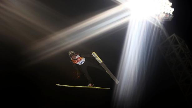 Ein Skispringer in der Luft unter hellen Scheinwerfern.
