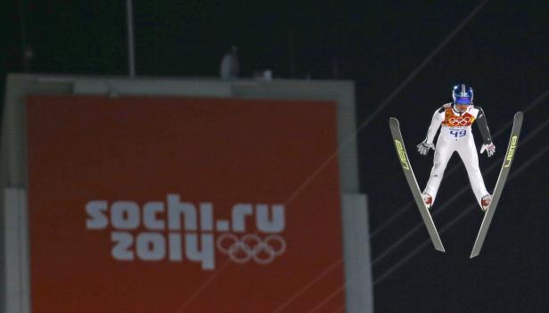 Eine Skispringerin in der Luft vor einem „Sochi 2014“-Logo.
