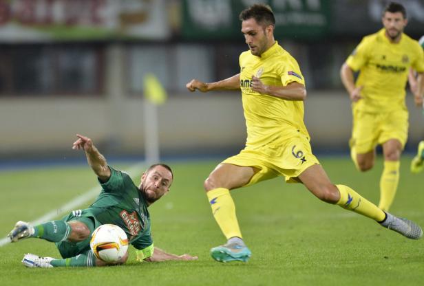Ein Fußballspieler in Grün liegt am Boden, während ein Spieler in Gelb den Ball führt.