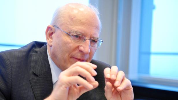 Ein älterer Mann mit Brille und Anzug gestikuliert mit den Händen.