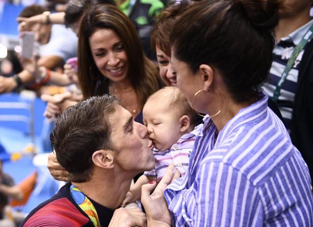Michael Phelps küsst sein Baby, während andere Personen zusehen.