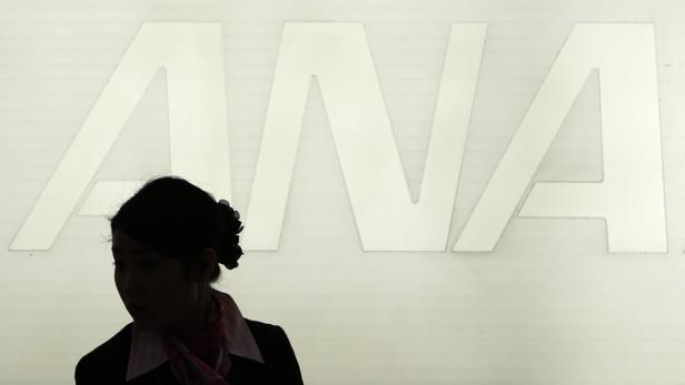 Eine Stewardess steht vor dem Logo der Fluggesellschaft ANA.
