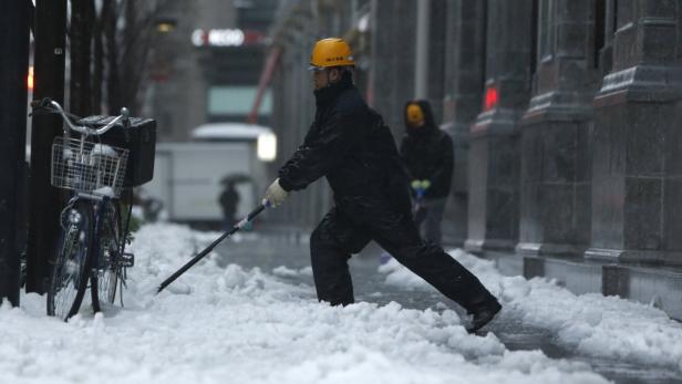 Ein Mann mit Schutzhelm schiebt Schnee auf einer Straße.