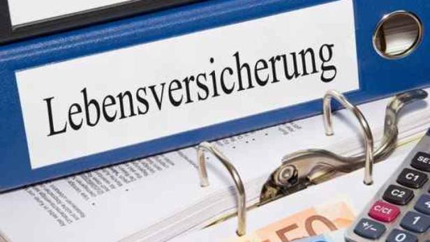 Ein blauer Ordner mit der Aufschrift „Lebensversicherung“ liegt auf Dokumenten und einem Taschenrechner.