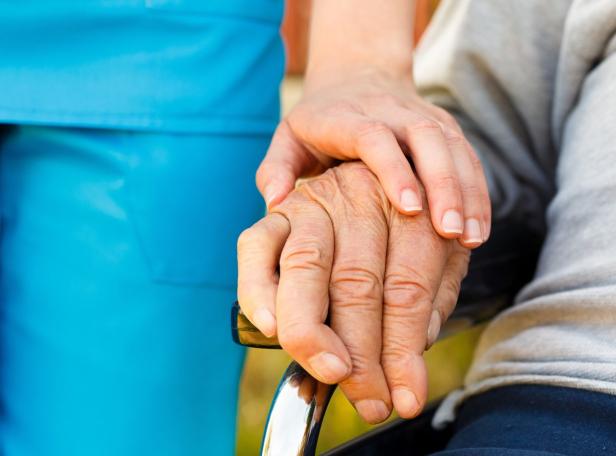 Eine junge Hand hält die Hand einer älteren Person im Rollstuhl.
