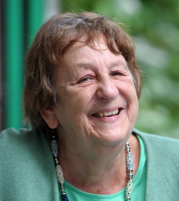 Eine ältere Frau lächelt mit einer Halskette und einem grünen Oberteil.