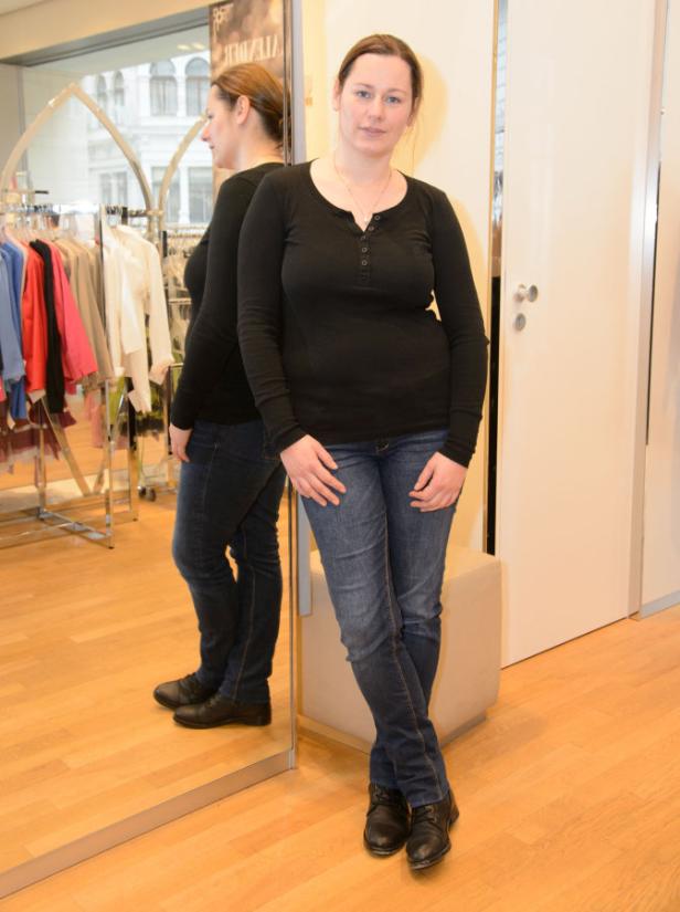 Eine Frau in Jeans und einem schwarzen Oberteil posiert vor einem Spiegel in einem Geschäft.