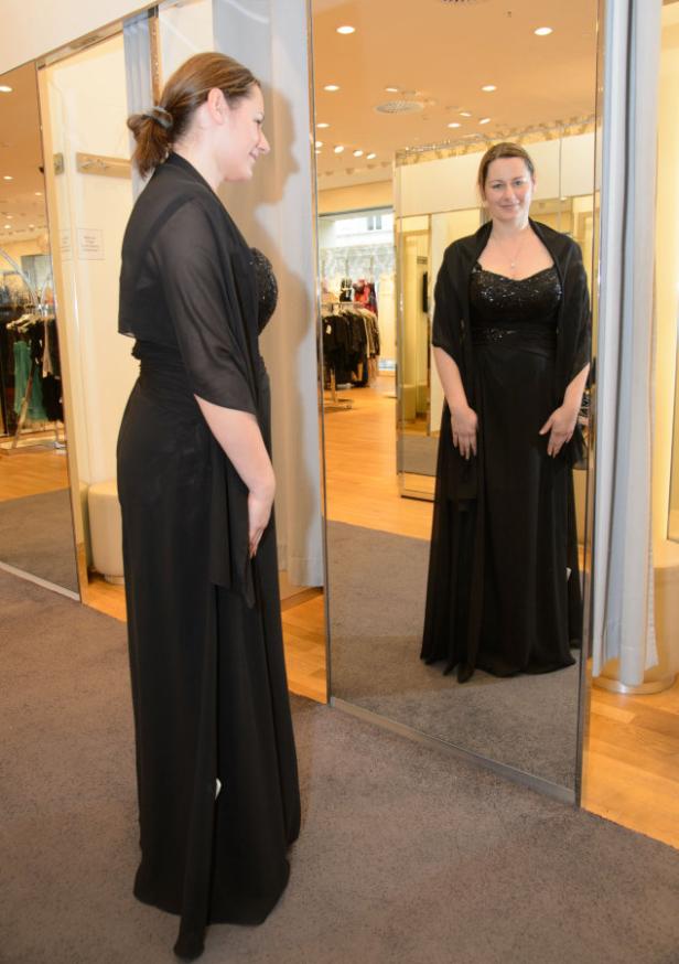 Eine Frau probiert ein schwarzes Abendkleid in einem Bekleidungsgeschäft an.