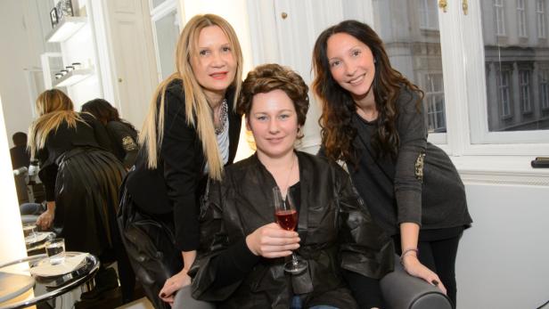 Drei Frauen posieren in einem Salon, eine hält ein Glas Rosé.