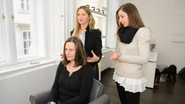Eine Frau sitzt im Friseurstuhl, während zwei Friseurinnen ihr Haar stylen.