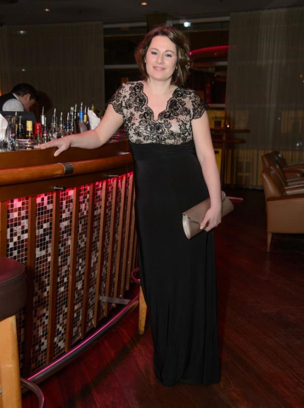 Eine Frau in einem schwarzen Abendkleid steht an einer Bar.