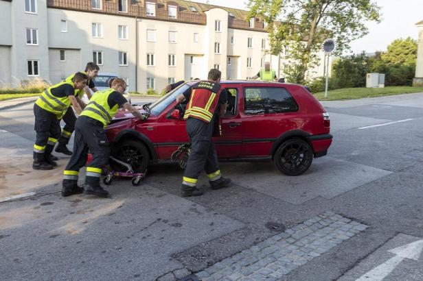 Rettungskräfte schieben ein beschädigtes rotes Auto von der Straße.